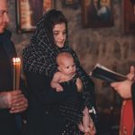 A touching moment during an Orthodox baptism ceremony with a priest, parents, and baby.