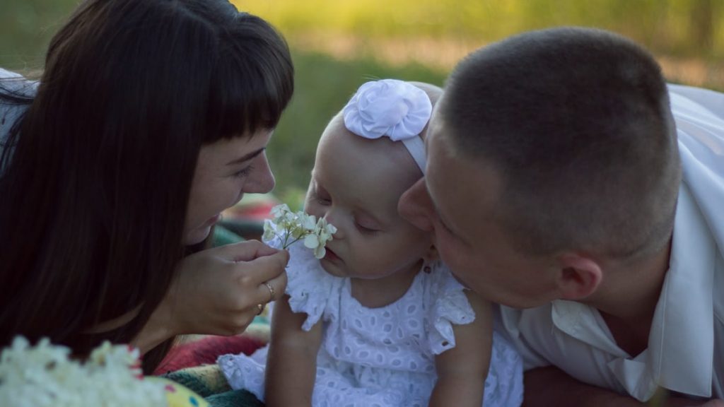 A loving family moment with parents and baby at a sunny outdoor picnic.