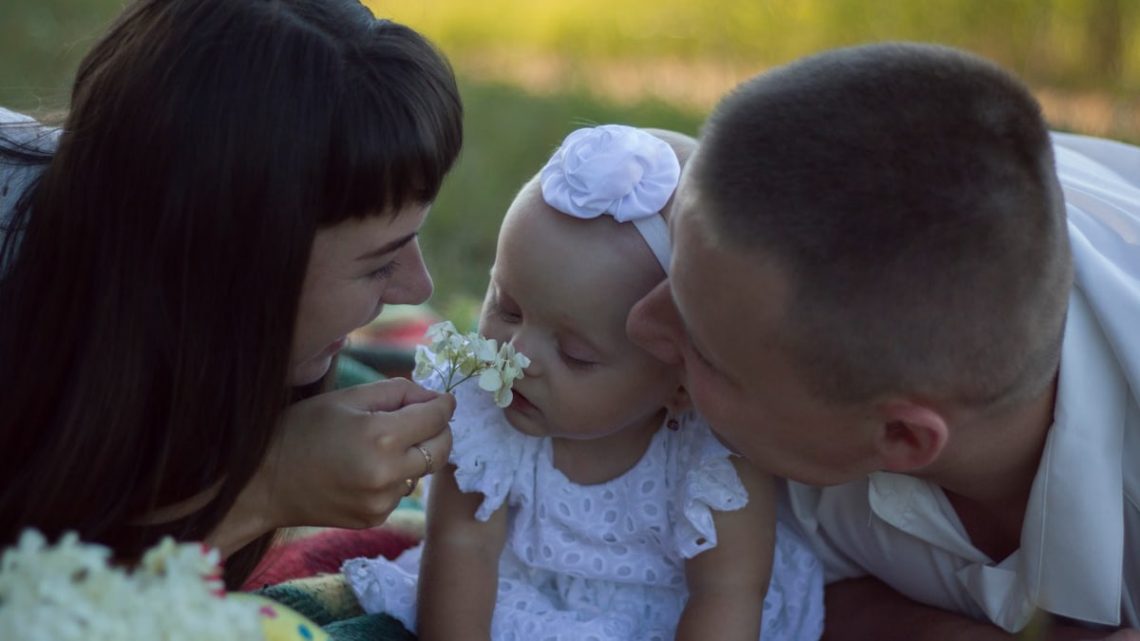 A loving family moment with parents and baby at a sunny outdoor picnic.