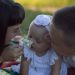 A loving family moment with parents and baby at a sunny outdoor picnic.