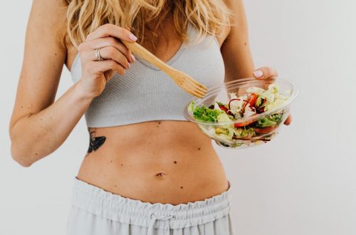 Young woman in sports attire holding a fresh salad bowl, promoting a healthy lifestyle.